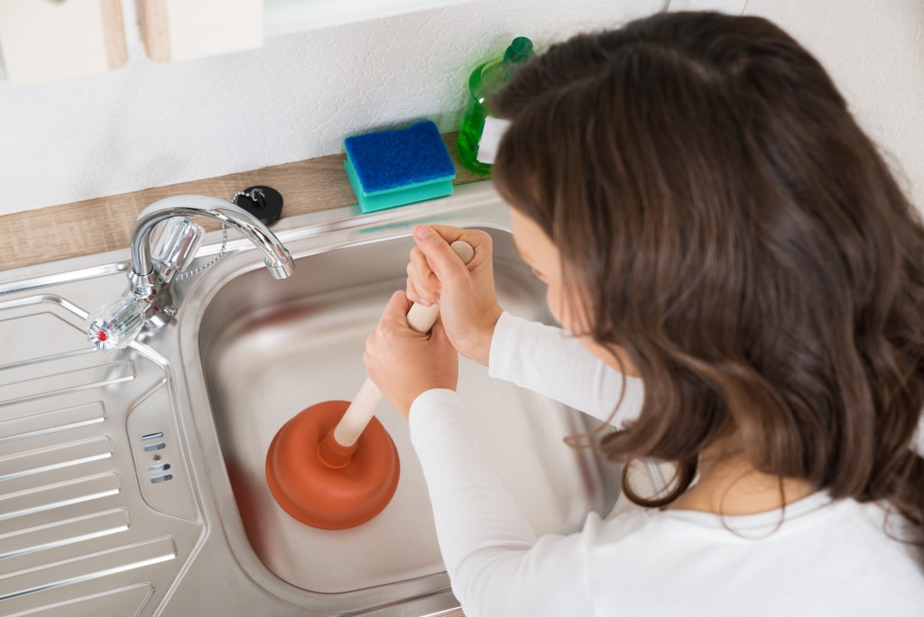 woman using a plunger to unclog drain