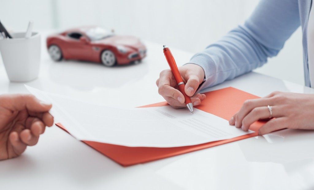 man signing a loan, a miniature red car on the background