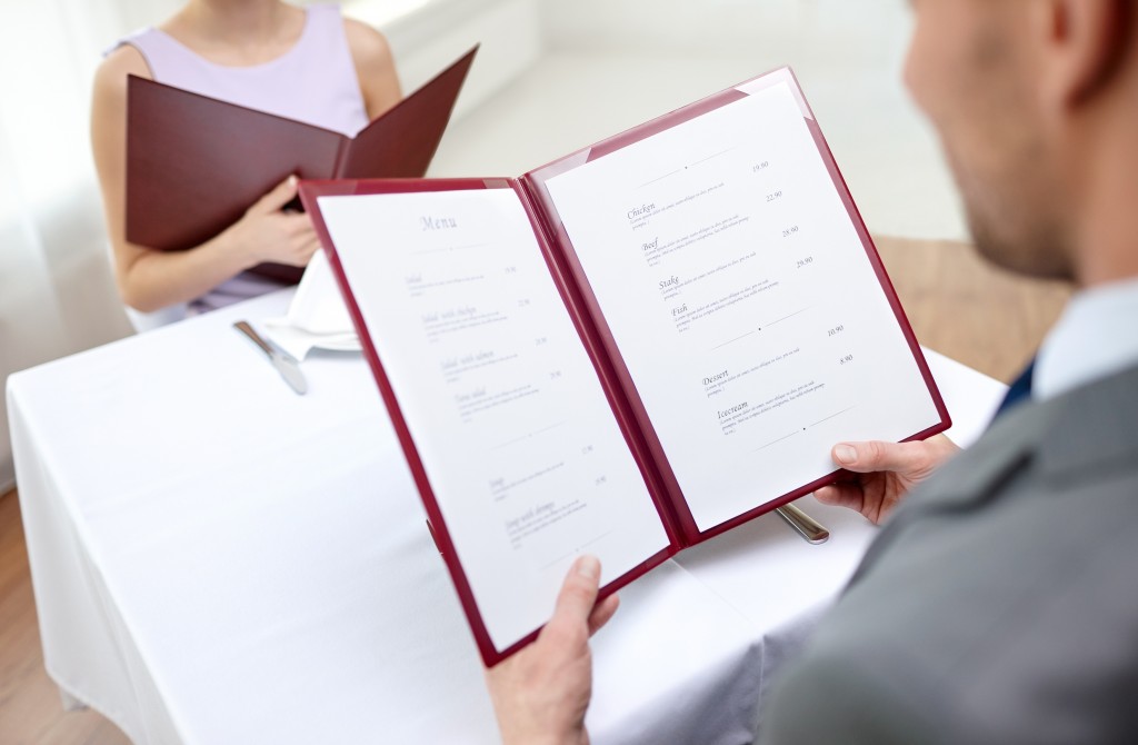 close up of couple with menu choosing dishes at restaurant